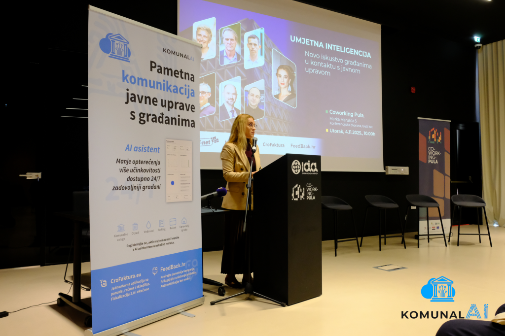 Voditeljica na podijumu o umjetnoj inteligenciji u javnoj upravi; ekran prikazuje "UMJETNA INTELIGENCIJA" sa slajdovima o kontaktu s građanima; plavi baneri Komunal Pula i CroFaktura u modernom co-workingu.