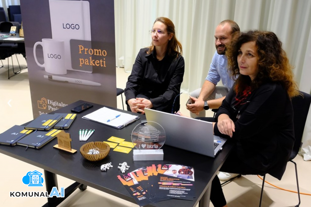 Tri člana tima sjede za crnim stolom prepunim promo materijala GT-neta, Digitalne Proizvodnje, Feedbacka i KomunalAI-a